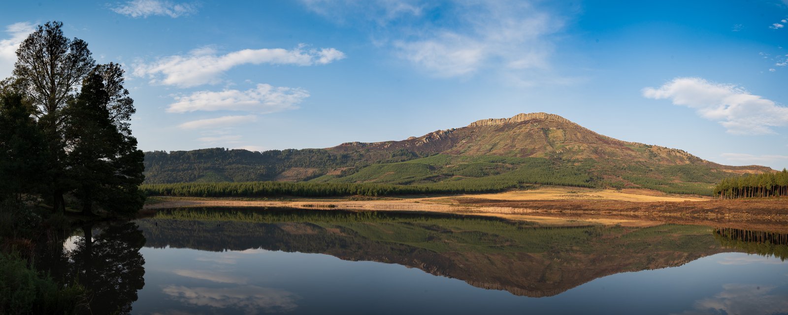 A mountain ridge reflected in still water beneath a blue Hogsback sky.