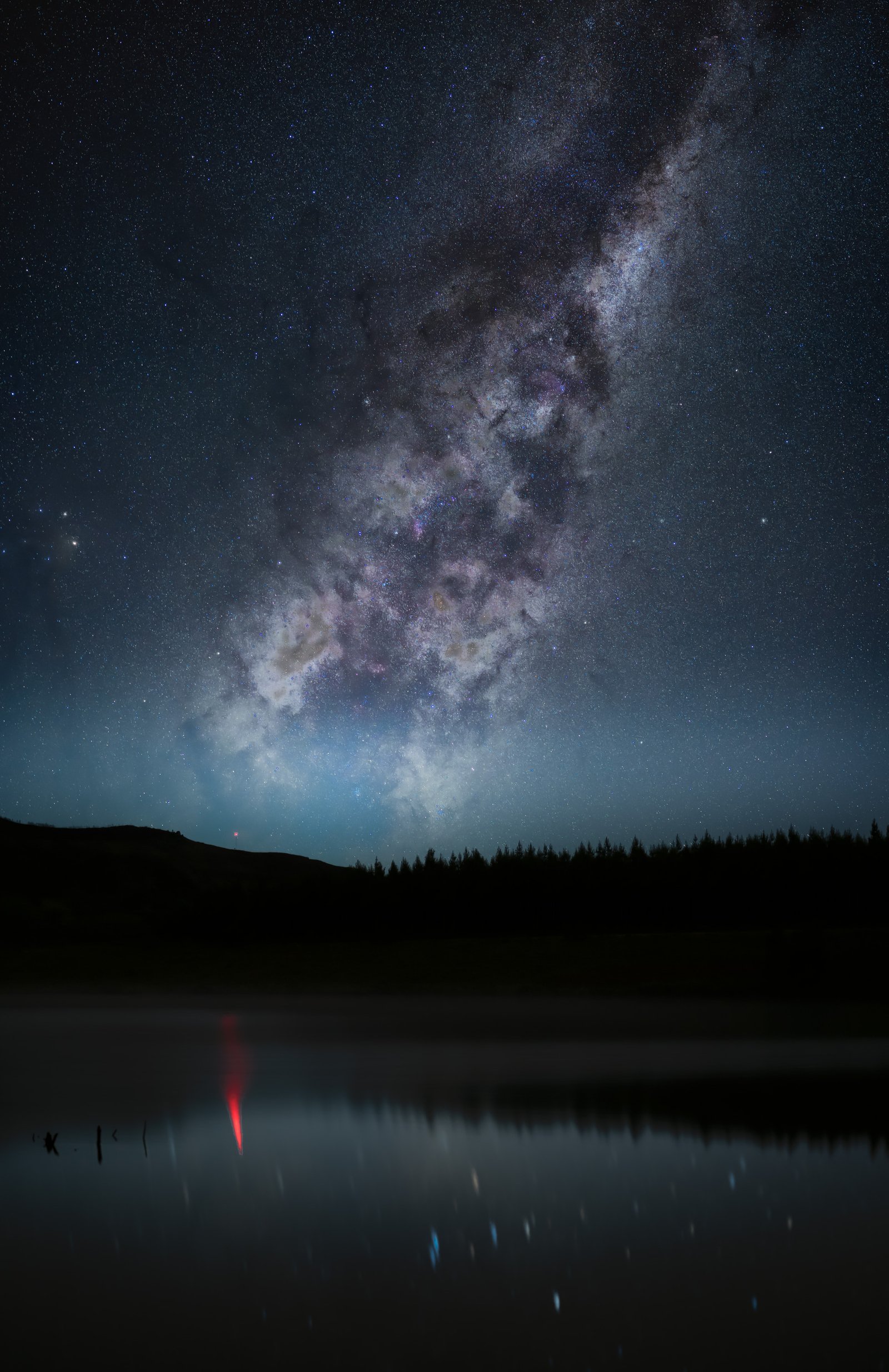 The Milky Way above a still lake and a dark tree line near Hogsback.