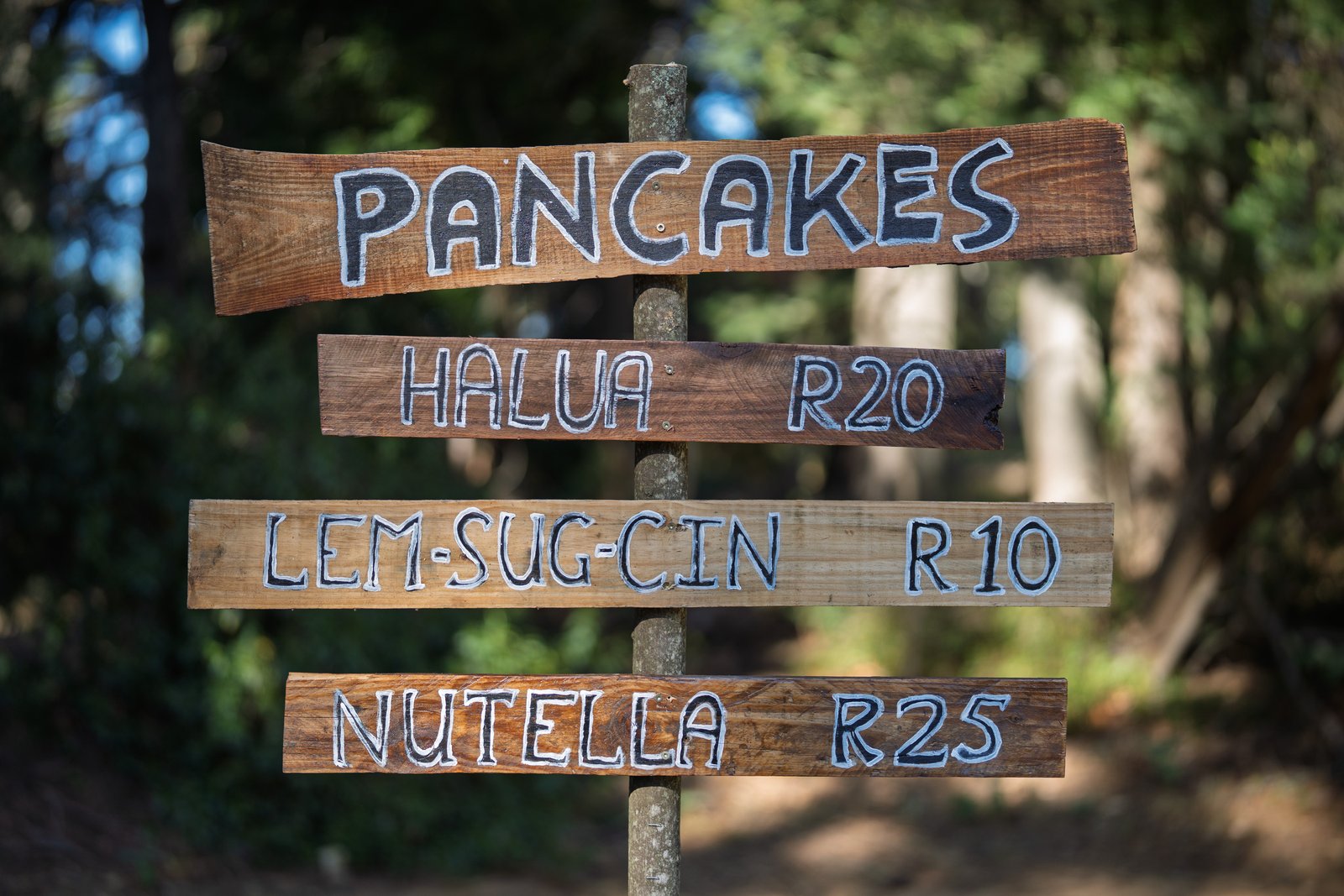 A hand-painted wooden pancake sign photographed in Hogsback; displayed prices are part of the photograph.